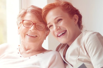 Happy elderly woman with caregiver smiling together